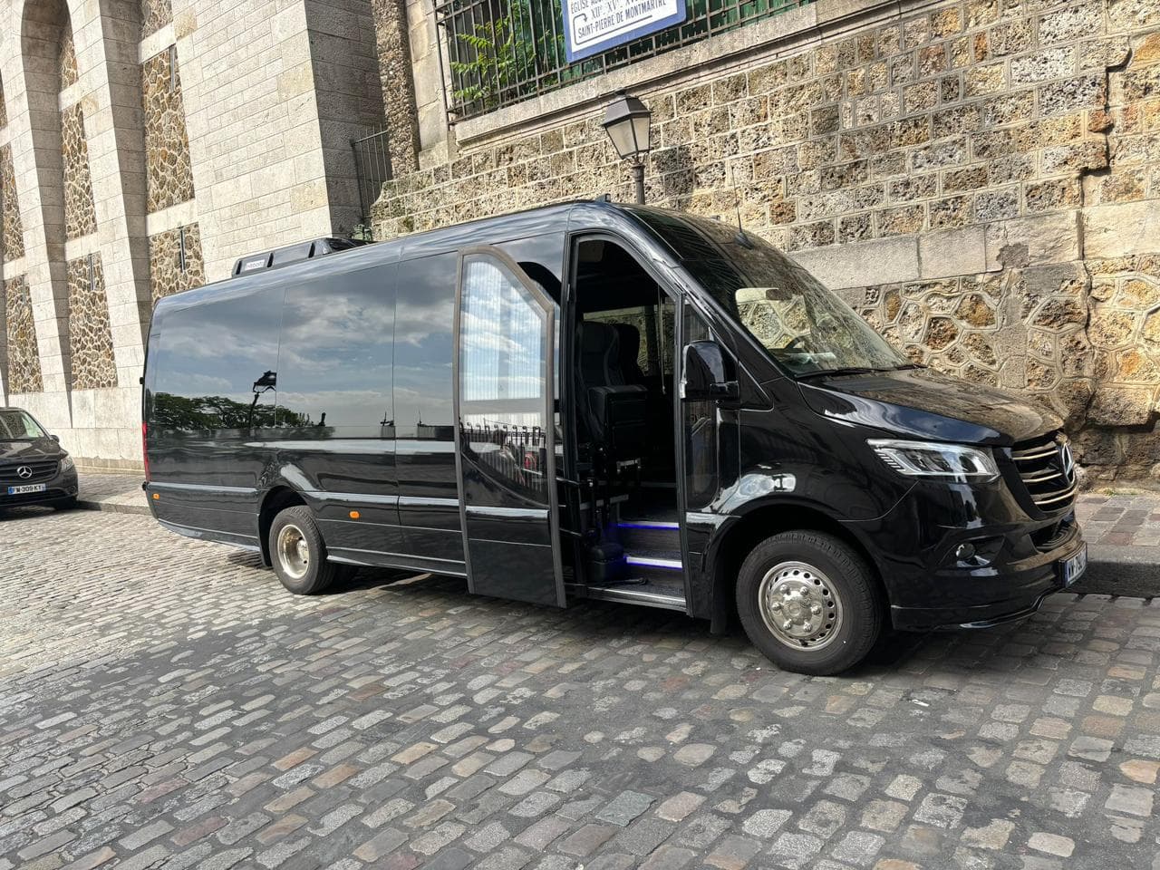 Minibus Mercedes Sprinter noir de profil, porte ouverte, rue pavée à Montmartre